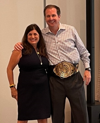 Chris Todd, the new CEO of UKG, is presented with a champion belt by Jennifer Brafman Staffen of UKG Corporate Communications during a June 2022 Analyst Relations event in Fort Lauderdale, FL